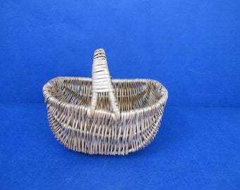 May include: A woven wicker basket with a handle. The basket is oval shaped and has a light brown color.