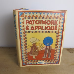 Peut inclure: Un livre vintage intitulé "Patchwork & Appliqué" avec une couverture jaune et une bordure de patchwork colorée. La couverture présente une illustration de deux enfants en vêtements vintage, l'un tenant un bouquet de fleurs.