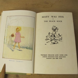 Pode incluir: Livro aberto com ilustrações e texto. A página esquerda mostra uma menina com um vestido rosa e uma cesta. A página direita diz "MARY WAS FIVE" e "THE BLACK ROCK". Publicado por THOMAS NELSON AND SONS LTD.