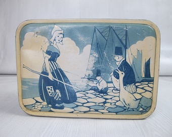 Vintage tin. Girl in her regional costume on a quayside with a fisherman, goose and sailing ships. Rectangular faded tin