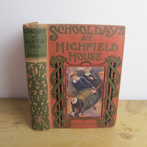 May include: A vintage book titled "School Days at Highfield House" by An M. Alan. The cover features a red background with green and black decorative borders. The illustration shows a group of boys playing with a barrel.