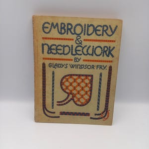 May include: Vintage book titled "Embroidery & Needlework" by Gladys Windsor Fry. The cover is tan with blue and orange lettering and decorative elements. A central design features a heart-shaped pattern in orange and brown.