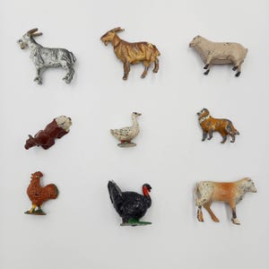 May include: A collection of nine small, vintage farm animal figurines. The set includes a goat, sheep, cow, dog, goose, rooster, and turkey. The figurines are painted in various colours, including brown, white, black, and orange.