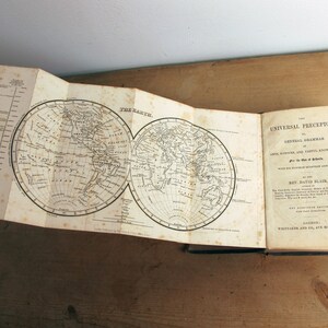 May include: An open book titled "The Universal Preceptor: or, General Grammar of Arts, Sciences, and Useful Knowledge, for the Use of Schools" by Rev. David Blair. The book features two maps of the world.