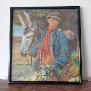 May include: A framed print depicting a person in a flat cap, blue jacket, and red polka-dot scarf standing beside a gray donkey. The person holds a woven basket filled with colorful wildflowers and greenery in a rural landscape setting.