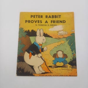 May include: Vintage children's book cover titled "Peter Rabbit Proves a Friend" by Thornton W. Burgess. The illustration features Peter Rabbit in a suit and a frog in overalls on a path. The cover is yellowed with age.