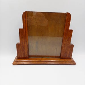 May include: A vintage wooden picture frame with a rectangular glass insert. The frame has a stepped design on the sides and a rectangular base. The wood has a warm, reddish-brown tone.