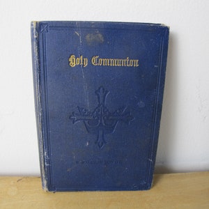 Op de afbeelding: Een blauw boek met de titel "Holy Communion" in gouden letters. Het boek heeft een kruisontwerp op de voorkant.