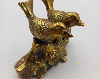 May include: Two gold-toned metal birds perched on a decorative base with floral details. The birds are facing each other and have detailed features.