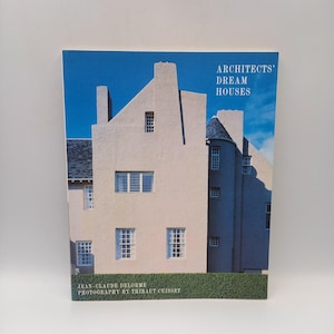 Op de afbeelding: Een boek met de titel "Architects' Dream Houses" met een foto van een lichtgekleurd gebouw met meerdere ramen en een blauwe lucht. De namen Jean-Claude Delorme en Thibaut Cuisset staan ook op de cover.