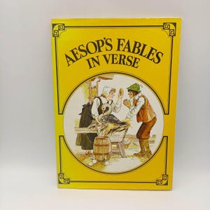 May include: A hardcover book titled "Aesop's Fables in Verse" with a yellow cover and decorative border. The cover features a circular illustration of two people in period clothing, with a swan and eggs. The book is in good condition.