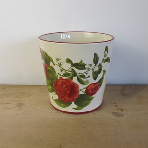 May include: White ceramic planter with a red rim and a floral design featuring red camellias and white flowers on green vines.