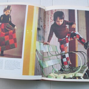 May include: A girl wearing a red and green checked skirt and a black turtleneck shirt. A boy wearing red and black checked trousers and a brown turtleneck shirt is standing on a green metal bench.