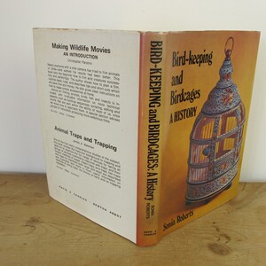 May include: Two book covers side-by-side. The cover on the left is for a book titled "Making Wildlife Movies: An Introduction" by Christopher Parsons. The cover on the right is for a book titled "Bird-keeping and Birdcages: A History" by Sonia Roberts. The cover features a detailed illustration of a birdcage with intricate designs and colorful enamel.