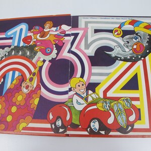 May include: A vintage children's book illustration featuring colorful numbers and whimsical characters. The artwork includes a clown, a car, a plane, and a smiling moon, all set against a dark purple background with rainbow and striped accents.