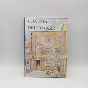 May include: A hardcover book titled "LONDON DELFTWARE" with an illustration of a brick building. The building has multiple windows, a doorway, and figures of people and a dog. The text "LONDON POTTERY ESTABLISHED 1731" is also visible.