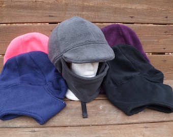 Puede incluir: Cuatro gorros de forro polar en diferentes colores. Un gorro gris con visera y mascarilla, un gorro rosa, un gorro azul marino y un gorro morado.