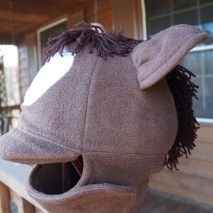 Puede incluir: Disfraz de cabeza de caballo de color marr&oacute;n de vell&oacute;n con un parche blanco en la cara y un sombrero de ala de vell&oacute;n marr&oacute;n. El disfraz tiene una crin y orejas de vell&oacute;n marr&oacute;n.
