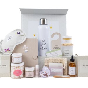 May include: A gift box filled with self-care items, including a white water bottle with the text "Be Cool Mama", a sleep mask, bath bombs, a candle, and a bar of soap. The box is decorated with a floral design.