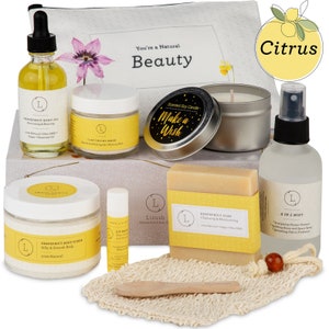May include: A citrus-themed gift set with a white and gray box, a white pouch, a grapefruit body oil, a clay facial mask, a scented soy candle, a grapefruit soap, a lip balm, a grapefruit body scrub, and a 2-in-1 mist. The box has the text "You're a Natural Beauty" on it. The candle has the text "Make a Wish" on it. The soap has the text "Grapefruit Soap Cleaning & Moisturizing 100% Natural Vegan + Bio-Oil" on it. The mist has the text "2 in 1 Mist Engaging Shower Steamer Refreshing Room and Space Spray Refreshing Fabric Freshener" on it.