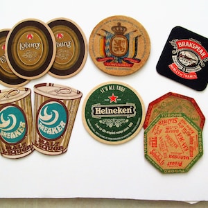 May include: A selection of beer coasters with various brand designs. The coasters are in different shapes, including round and square. Brands include "Loburg", "Heineken", and "BrakSpear". The colours are brown, green, and black.