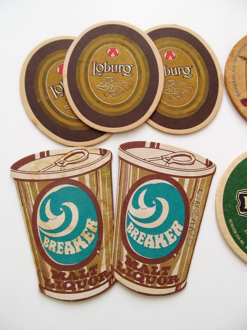 May include: A selection of vintage beer mats and malt liquor cutouts. The mats have a brown and gold design with the word "Loburg". The malt liquor cutouts are shaped like cans with the word "Breaker" and a teal wave design.