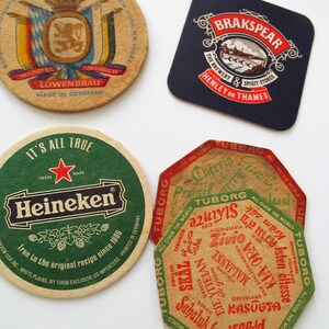May include: A selection of vintage beer mats with brewery branding. The mats display logos and text for Lowenbrau, Brakspear, Heineken, and Tuborg. The shapes vary, including round, square, and octagonal, with diverse colors and designs.