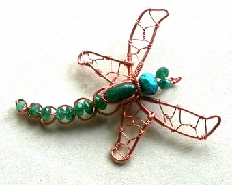 May include: A copper wire dragonfly with green and turquoise gemstone accents. The dragonfly's wings are made of wire and the body is adorned with green gemstones. The dragonfly's tail is made of a string of green gemstones.