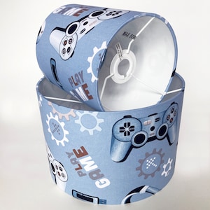 May include: Two blue lampshades with a gamer theme. The lampshades feature a pattern of video game controllers, gears, and the text "Play Game".