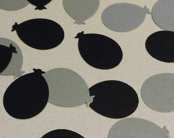 May include: A scattering of black and silver balloon confetti. The balloons are cut out in the shape of a balloon with a rounded bottom and a pointed top.