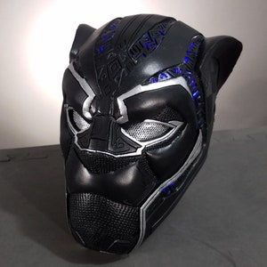 Puede incluir: Máscara de Black Panther de plástico negro y plateado con luces LED azules. La máscara tiene un diseño detallado con una superficie texturizada.