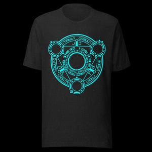 Op de afbeelding: Een donkergrijs T-shirt met een blauw cirkelvormig ontwerp met een symbool met de tekst "GRIMULA GRIMULA" en andere tekst in een cirkelvormig patroon.