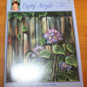 May include: A softcover instructional art book titled Enjoy Acrylic Scheewe Art Workshop by Susan Scheewe Brown. The cover features a painting of purple hydrangea flowers growing against a weathered wooden fence with green leaves.