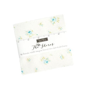 May include: A square fabric bundle with a floral pattern in shades of blue and yellow on a white background. The text "The Shores" is visible, along with a ruler graphic. The fabric is likely for quilting or crafting.