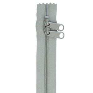 May include: A light gray double-pull zipper with two sliders. The zipper teeth are a matching light gray color. The sliders have a rounded shape with a hole for easy gripping. The zipper is shown against a white background.