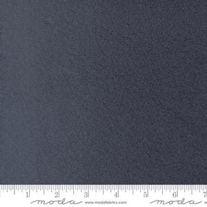 May include: A close-up of a piece of dark blue fabric with a textured surface. The fabric has a subtle, mottled appearance. A ruler is at the bottom of the image, with the Moda Fabrics logo and website address.