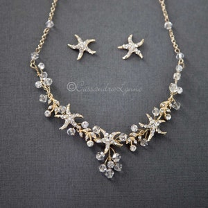 May include: Gold necklace and earrings set with clear crystal beads and starfish charms. The necklace features a cascading design with multiple starfish charms and crystal beads.