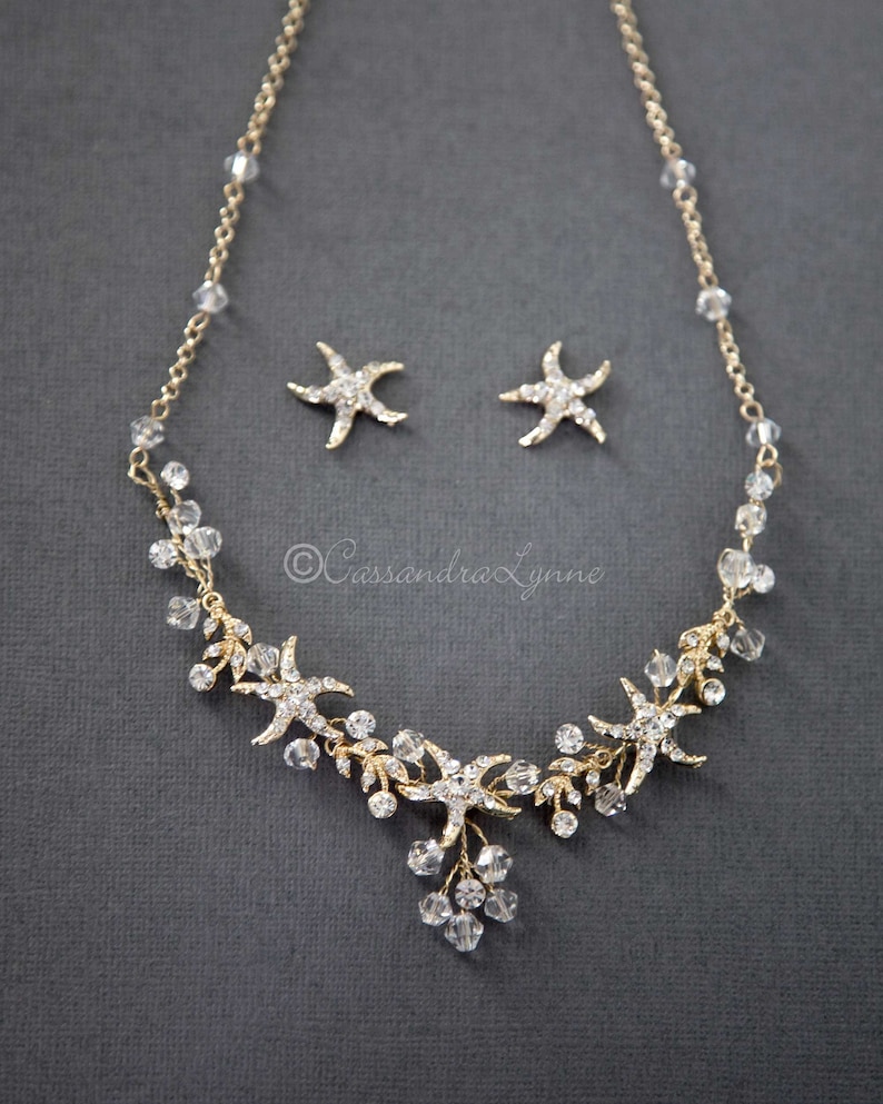 May include: Gold necklace and earrings set with clear crystal beads and starfish charms. The necklace features a cascading design with multiple starfish charms and crystal beads.