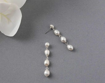 May include: A pair of silver dangle earrings with white pearl drops. Each earring has five pearls, decreasing in size from top to bottom.