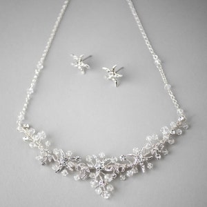 May include: A silver necklace and earrings set with a delicate design of crystal starfish and vines. The necklace features a delicate chain with crystal accents.