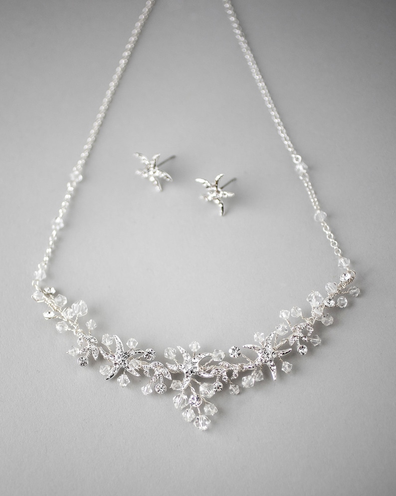 May include: A silver necklace and earrings set with a delicate design of crystal starfish and vines. The necklace features a delicate chain with crystal accents.