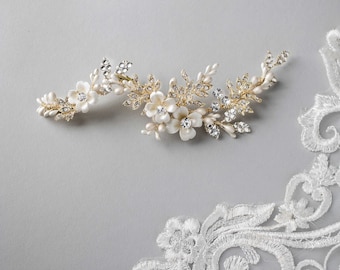 May include: Gold bridal hair comb with white pearl and crystal flowers. The comb has a delicate floral design with leaves and branches.