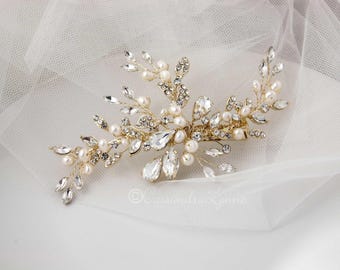 Op de afbeelding: Een goudkleurige haarspeld met een bloemmotief. Het is versierd met heldere kristallen, imitatieparels en kleine strass-steentjes. Dit haaraccessoire is ontworpen voor speciale gelegenheden en wordt in het haar gedragen.