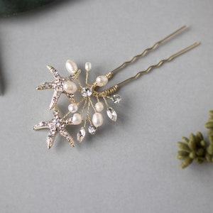 May include: Two gold starfish hair pins with pearl and crystal accents. The pins are attached to a gold wire base.