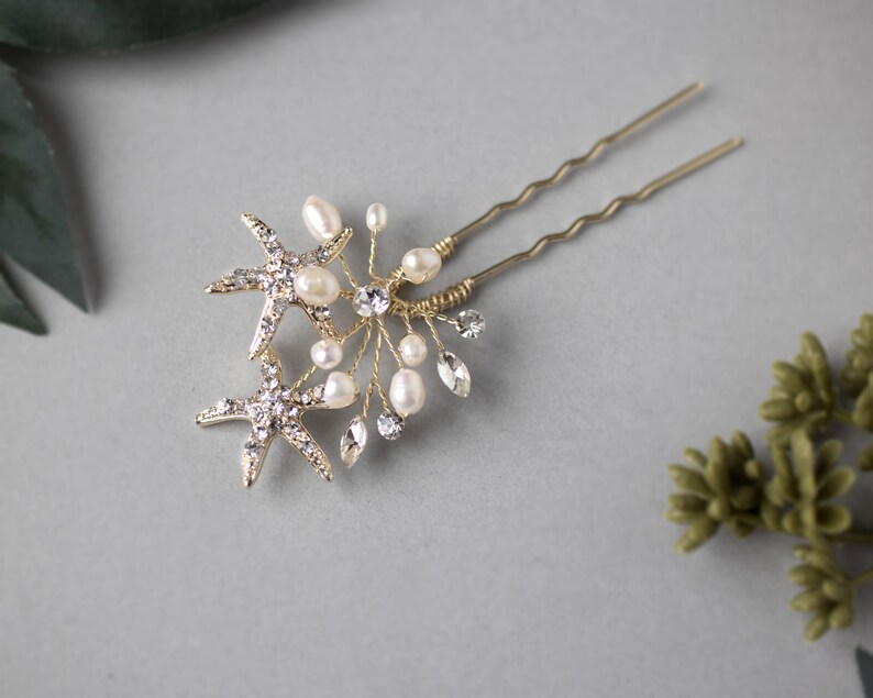 May include: Two gold starfish hair pins with pearl and crystal accents. The pins are attached to a gold wire base.