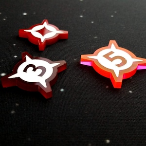 May include: Three red plastic game pieces with white star and number designs. The pieces are numbered 3 and 5. One piece has a white star in the center.