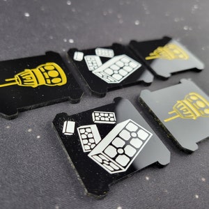 May include: Five black square game pieces with different yellow and white icons. The icons include a tower, a pile of bricks, and a single brick.