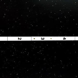 May include: A black and white image of a numbered scale with two small, light brown dots on the scale. The scale is numbered 1 through 5.