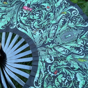 May include: A folding hand fan with black ribs and a dark fabric leaf featuring a light green botanical pattern of swirling leaves, various beetles, and a central keyhole motif. The design includes small red ladybugs and detailed insect illustrations.