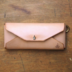 May include: A light brown leather wallet with a flap closure and a small metal snap. The wallet has a triangle logo with the text "Aomori Bless" on the front.